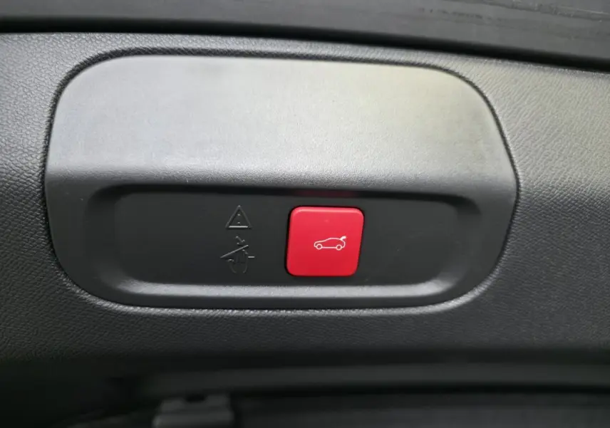 Gros plan sur le bouton rouge d'ouverture motorisée du hayon dans l'intérieur noir du Peugeot 408 gris Selenium.
