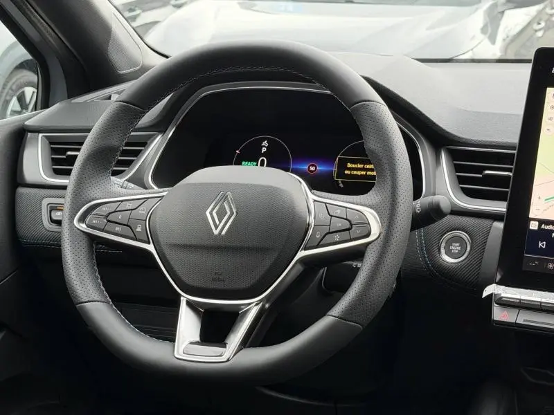 Vue rapprochée du volant cuir noir avec logo Renault et tableau de bord numérique du Captur hybride 2026.