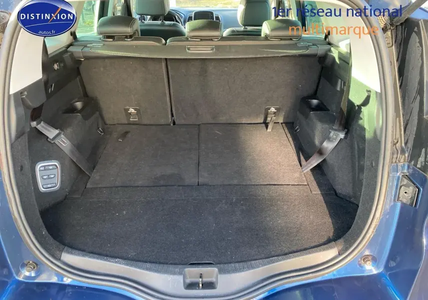 Coffre ouvert d’un Renault Grand Scénic IV bleu, montrant les sièges arrière rabattus et la moquette noire.