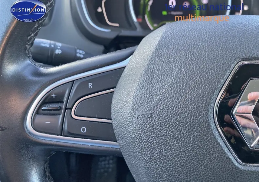 Gros plan sur le volant cuir de la Renault Grand Scenic IV bleu, avec commandes intégrées à gauche et logo Renault visible.