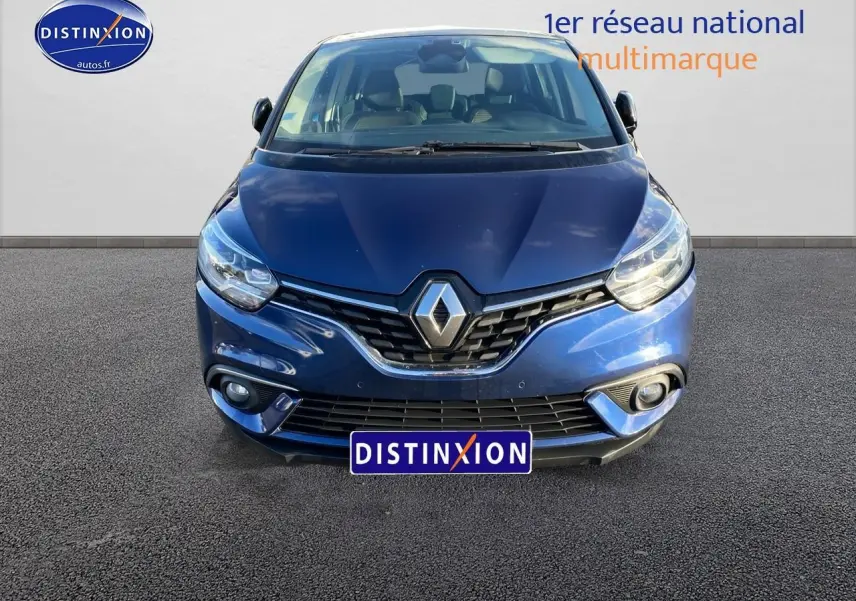 Vue avant d’un Renault Grand Scénic IV bleu avec calandre chromée et feux LED allumés sur fond neutre.