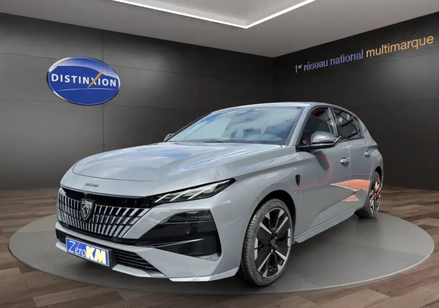 Peugeot 308 gris clair en vue 3/4 avant droit, avec calandre distinctive et jantes noires bicolores.