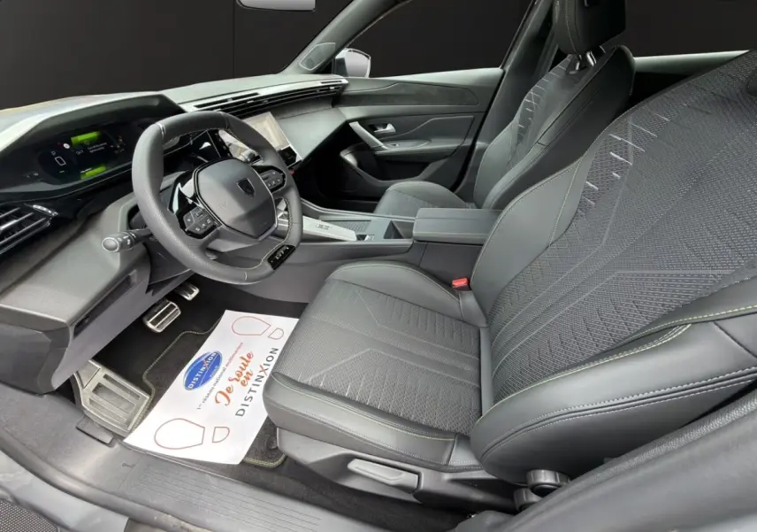 Intérieur avant droit de la Peugeot 308 gris clair, sièges tissu et cuir avec surpiqûres vertes, tableau de bord moderne.