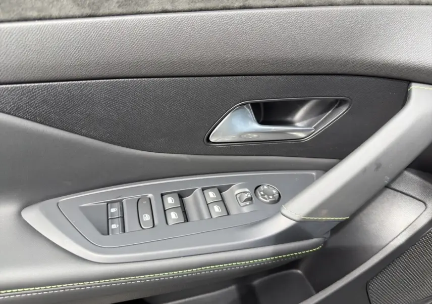 Gros plan sur la porte côté conducteur de la Peugeot 308 gris clair, avec commandes électriques et surpiqûres vertes.