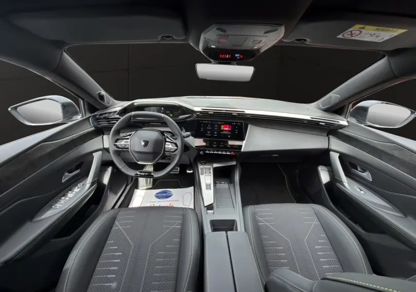 Vue intérieure avant de la Peugeot 308 2026, sièges noirs et tableau de bord moderne avec écran tactile central.