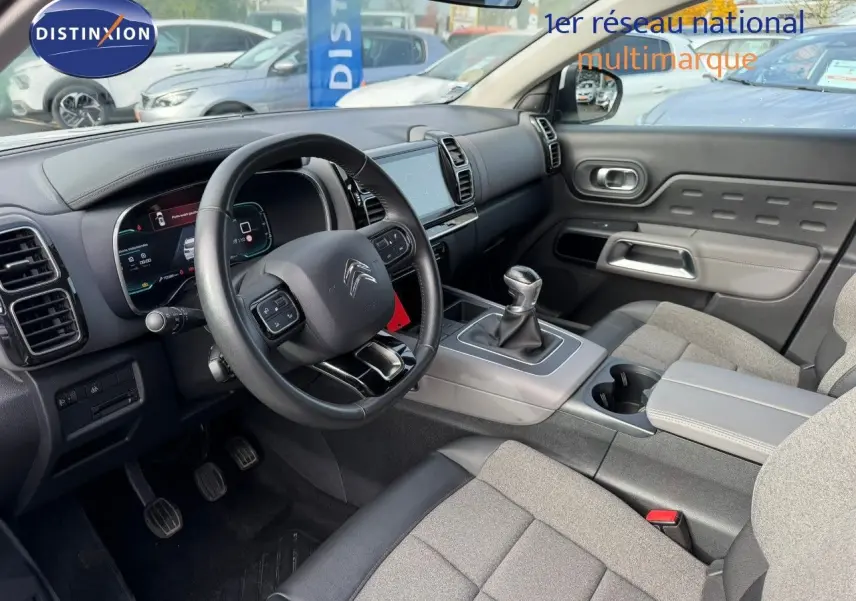 Vue intérieure côté conducteur du Citroën C5 Aircross 2019, volant cuir noir et sièges tissu gris avec console centrale grise.
