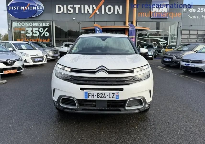 Vue de face d'un Citroën C5 Aircross blanc nacré, avec calandre distinctive et phares LED allumés, sur parking de concession.