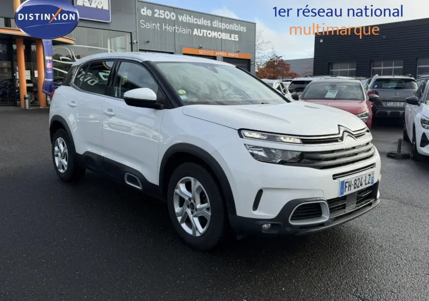 SUV Citroën C5 Aircross blanc nacré vu en 3/4 avant droit sur parking devant concession automobile.