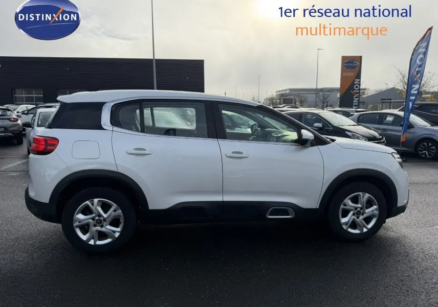 Profil latéral droit d'un Citroën C5 Aircross blanc nacré avec jantes alliage et protections noires sur un parking extérieur.