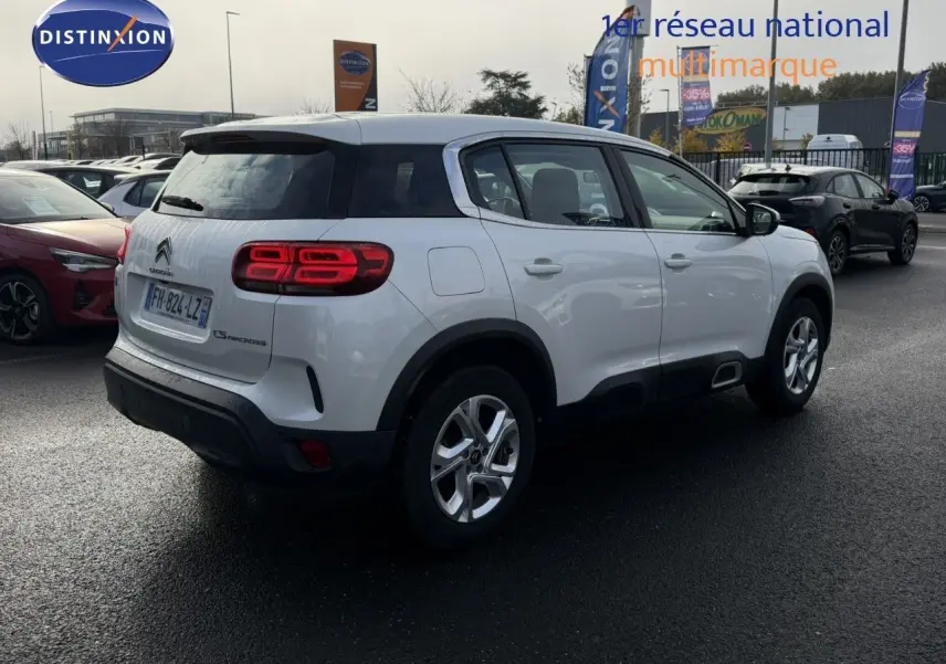 Vue 3/4 arrière droite d'un Citroën C5 Aircross blanc nacré avec feux arrière allumés sur parking extérieur.