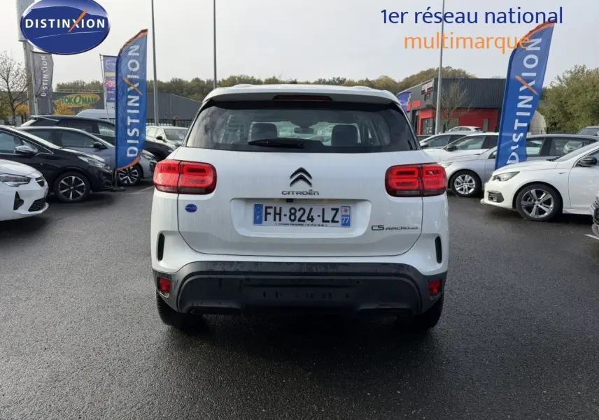 Vue arrière d'un Citroën C5 Aircross blanc nacré garé sur un parking, avec feux arrière allumés et plaques visibles.