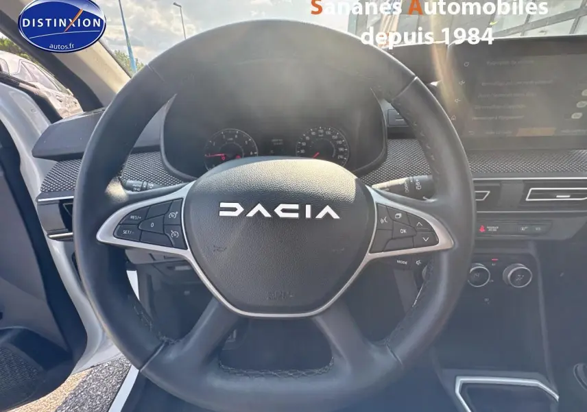 Vue intérieure centrée sur le volant noir DACIA du Jogger blanc, avec tableau de bord et écran tactile visibles à droite.