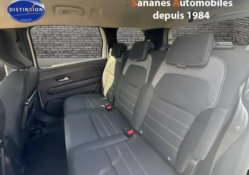 Vue intérieure du siège arrière droit du Dacia Jogger blanc, montrant la banquette trois places en tissu noir avec surpiqûres blanches.