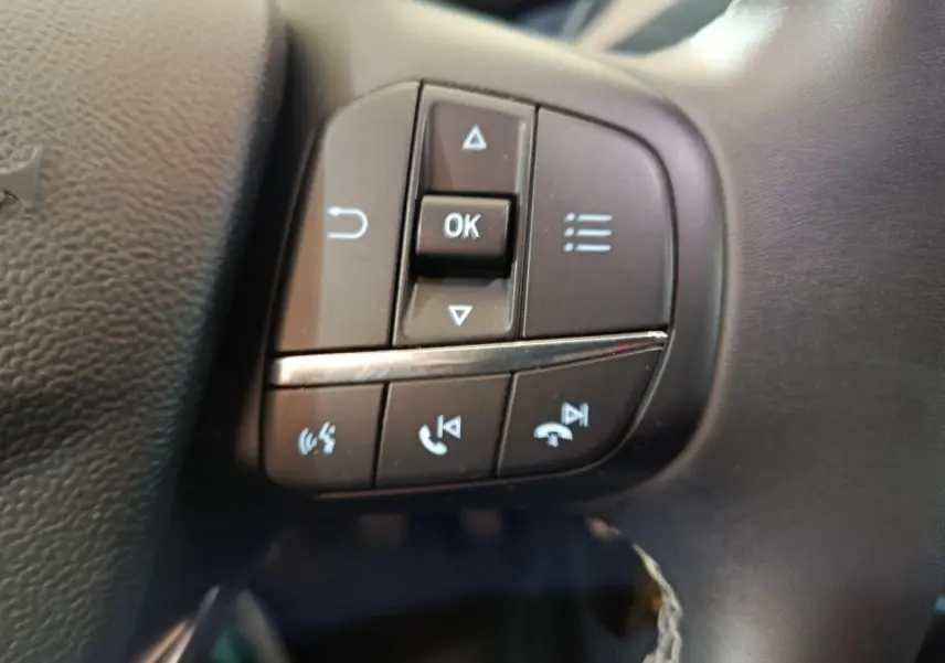 Gros plan sur les commandes multifonctions noires du volant en cuir d'une Ford Puma blanche, version Titanium 2022.