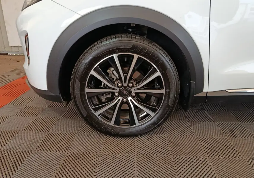 Gros plan sur la roue avant gauche noire et argentée du Ford Puma blanc, avec passage de roue en plastique noir.