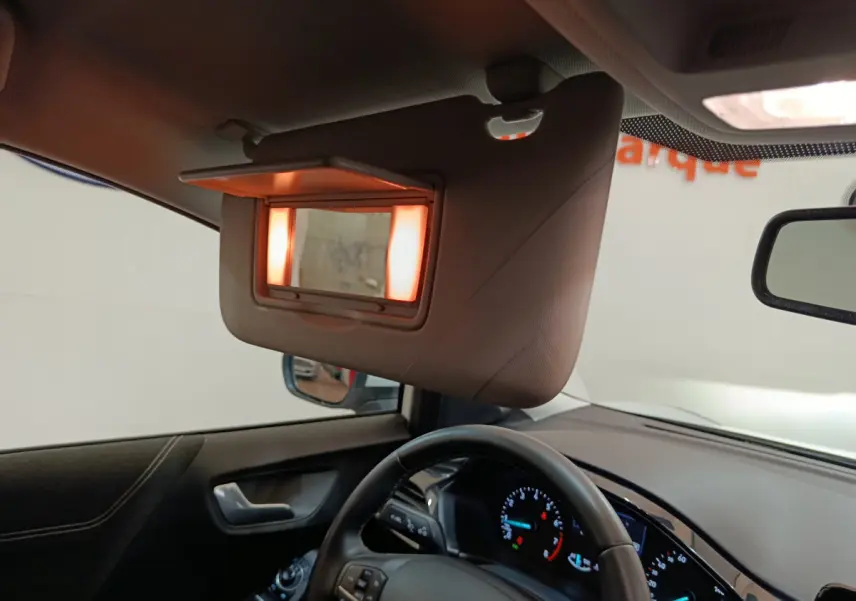 Intérieur du Ford Puma 2022 blanc, vue côté conducteur sur le volant, tableau de bord et miroir de soleil éclairé.