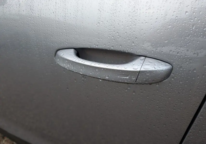 Poignée de porte gris métallisé du Peugeot 5008 2025, couverte de gouttes de pluie, vue en gros plan.