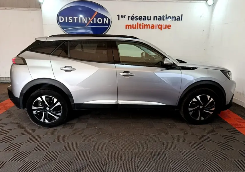 Profil droit d'un Peugeot 2008 gris clair 2021, avec jantes noires et toit noir contrasté en intérieur showroom.