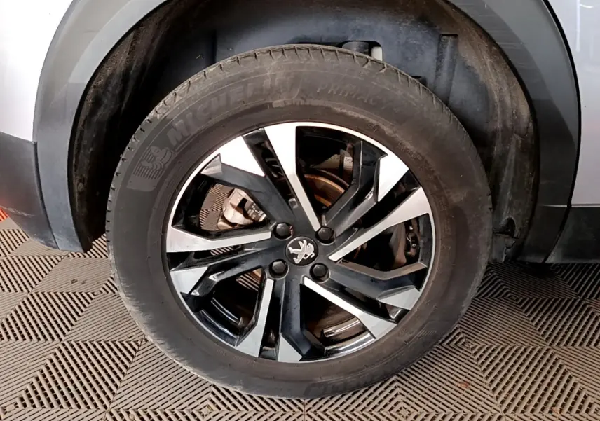 Gros plan sur la roue avant droite d’un Peugeot 2008 gris clair, avec jante alliage noire et argentée.