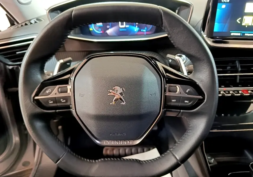 Vue rapprochée du volant cuir noir de la Peugeot 2008 avec commandes intégrées et tableau de bord numérique en arrière-plan.