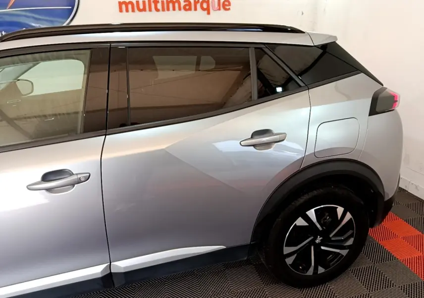 Vue latérale droite du Peugeot 2008 gris clair, mettant en valeur les vitres teintées et les jantes noires à motifs argentés.
