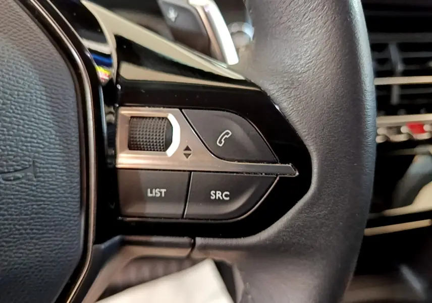 Gros plan sur les commandes gauche du volant cuir noir du Peugeot 2008 gris clair, avec boutons de téléphone et liste.