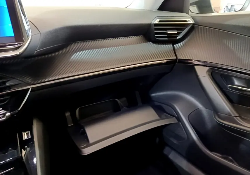 Intérieur côté passager du Peugeot 2008 gris clair 2021, tableau de bord avec finition carbone et boîte à gants ouverte.