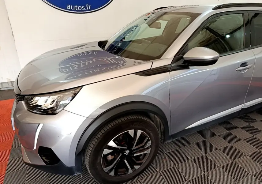 Vue 3/4 avant droit d’un Peugeot 2008 gris clair avec jantes noires et feux LED diurnes allumés.