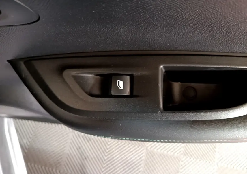 Gros plan sur le bouton de commande de vitre électrique côté conducteur dans l'habitacle noir d'une Peugeot 2008 gris clair.