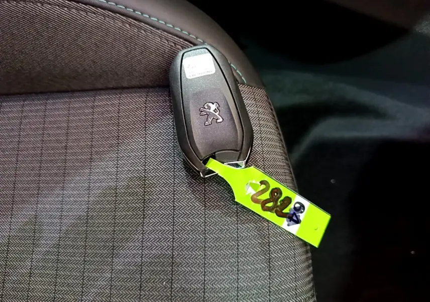 Gros plan sur la clé Peugeot posée sur un siège en tissu gris foncé à motifs, intérieur du Peugeot 2008 2021.
