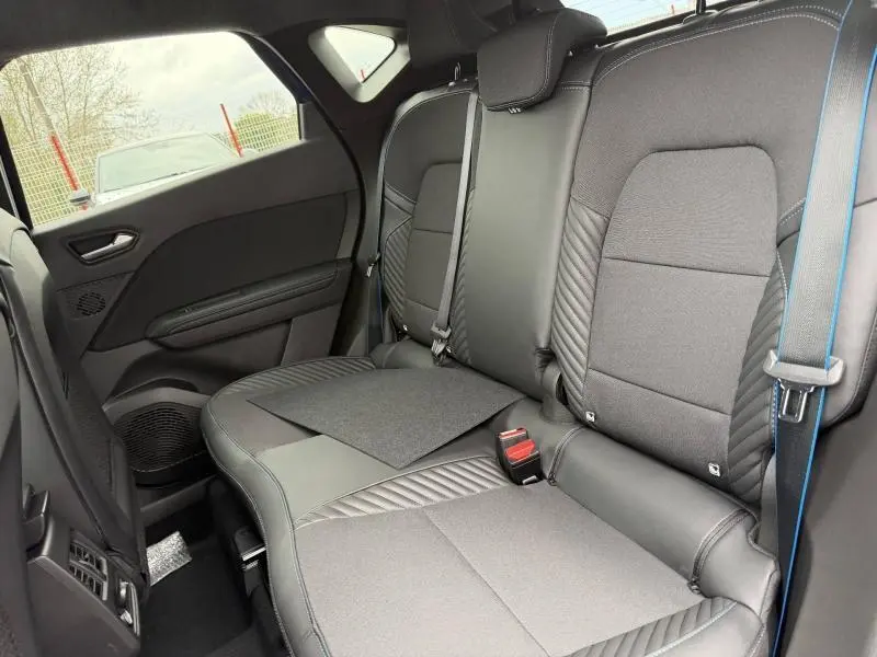Vue intérieure arrière côté droit du Renault Captur 2026, sièges noirs avec surpiqûres bleues et ceinture bleue visible.