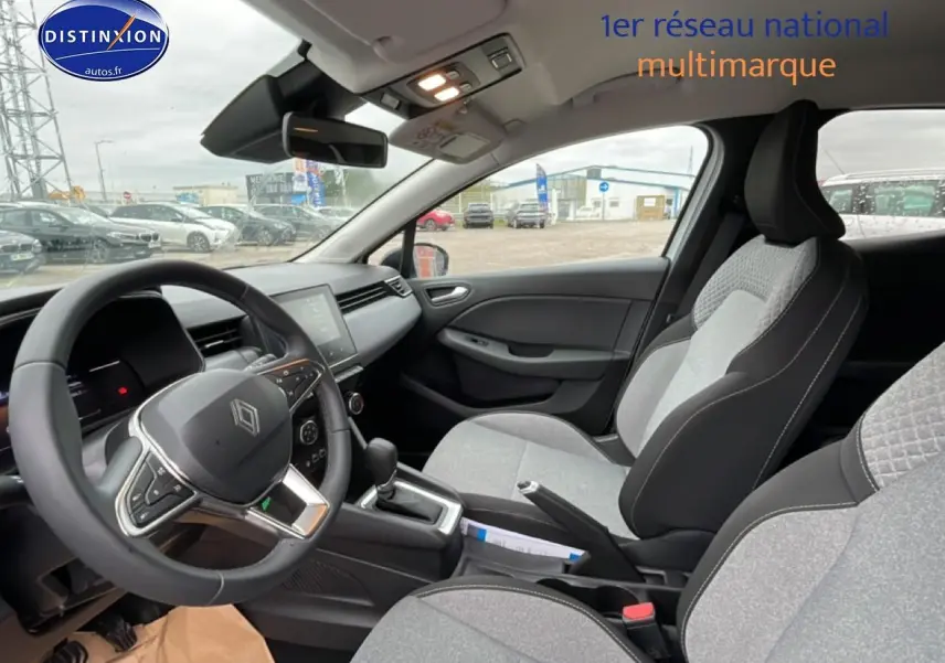 Vue intérieure côté conducteur de la Renault Clio V 2025 avec sièges gris à motif 3D et volant multifonction.