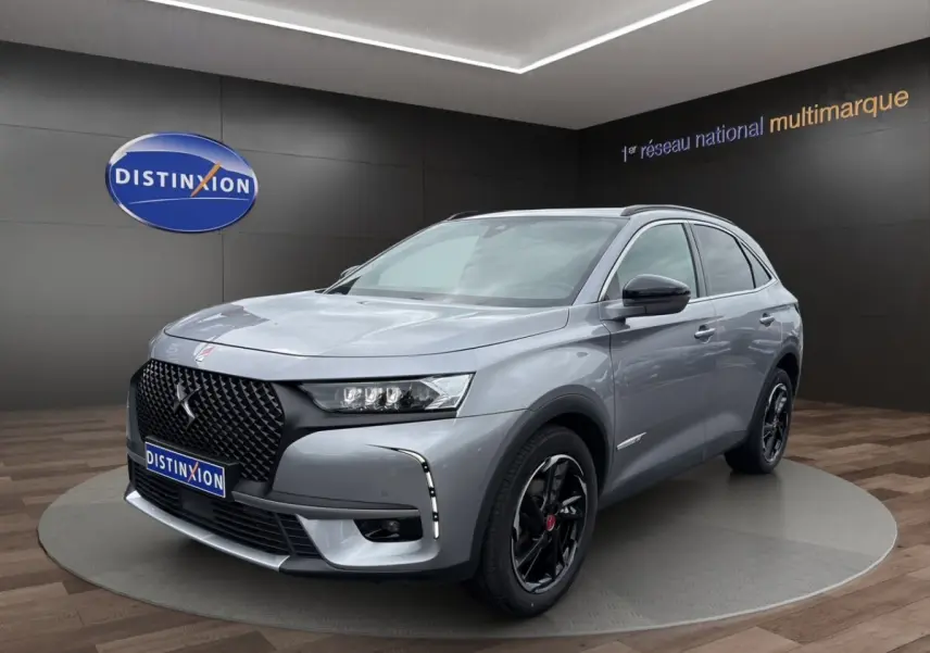 Vue 3/4 avant droit d'un DS7 Crossback gris clair avec calandre noire et jantes noires brillantes dans un showroom.