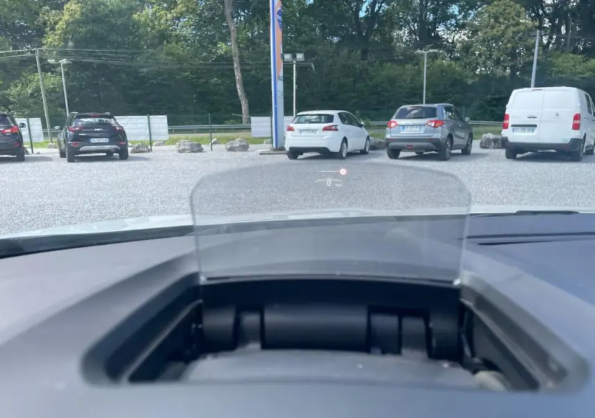 Affichage tête haute visible depuis l'intérieur d'une Renault Mégane IV blanche, vue avant sur un parking extérieur.