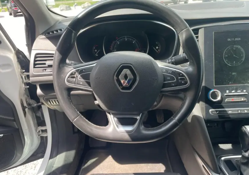 Vue intérieure centrée sur le volant noir de la Renault Mégane IV blanche, avec tableau de bord et écran tactile visibles.
