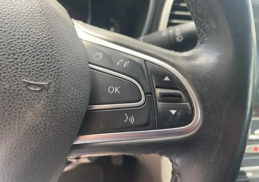 Gros plan sur les commandes multifonctions à droite du volant noir de la Renault Mégane IV blanche de 2016.