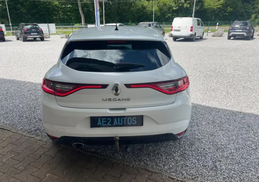 Vue arrière d'une Renault Mégane IV blanche de 2016 avec feux LED allumés et attelage visible.