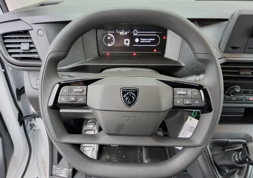 Vue rapprochée du volant noir du Peugeot Expert Fourgon blanc 2025 avec tableau de bord numérique et commande au volant.