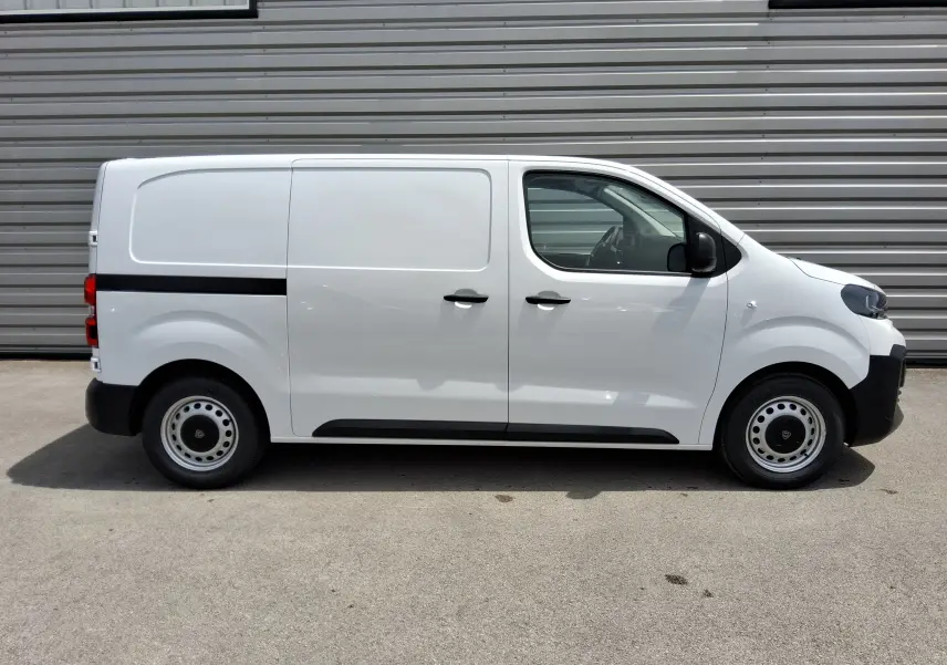 Vue latérale droite d’un Peugeot Expert Fourgon blanc 2025 avec bande noire et roues acier, stationné devant un mur métallique.