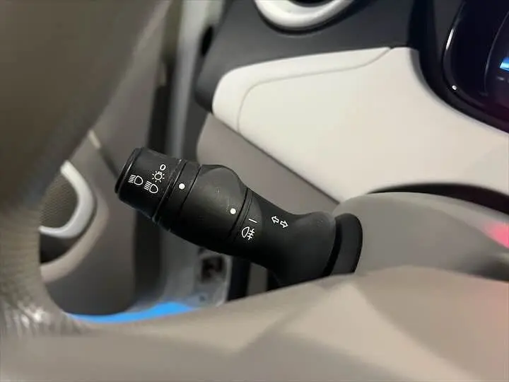 Gros plan sur la commande des phares et clignotants à gauche du volant dans l’habitacle clair d’une Renault ZOE blanc glacier.