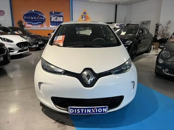 Vue de face d'une Renault ZOE blanche glacier exposée en showroom avec logo Distinxion sur la plaque avant.