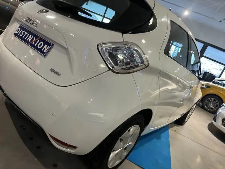 Vue 3/4 arrière droite d'une Renault ZOE blanche glacier exposée en showroom avec plaque Distinxion visible.