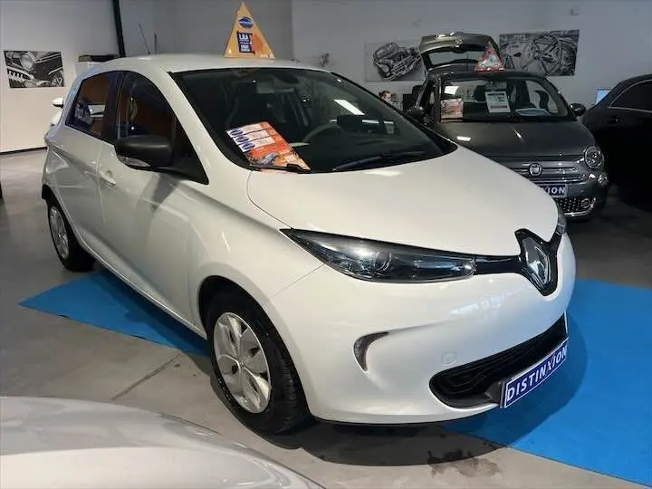 Renault ZOE blanc glacier vue 3/4 avant droit dans un showroom avec panneau promotionnel sur le toit.