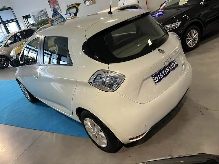 Vue 3/4 arrière droite d'une Renault ZOE blanche glacier exposée en showroom avec plaque Distinxion visible.