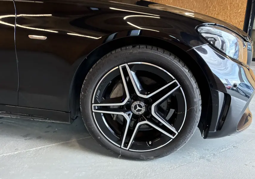 Gros plan sur la roue avant gauche noire à jante AMG bi-ton d'une Mercedes Classe C Break noir métal.