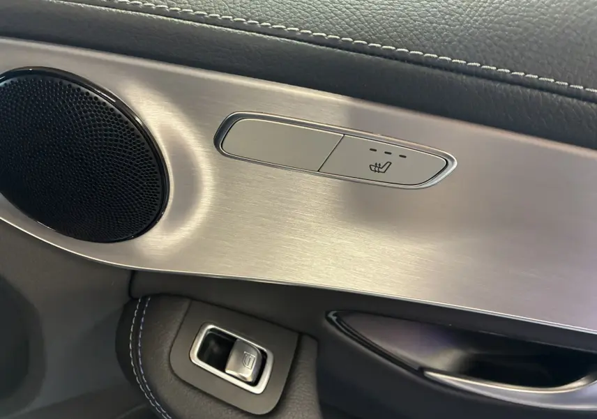 Détail du bouton de siège chauffant et haut-parleur sur la garniture intérieure côté gauche d'une Mercedes Classe C Break noire.