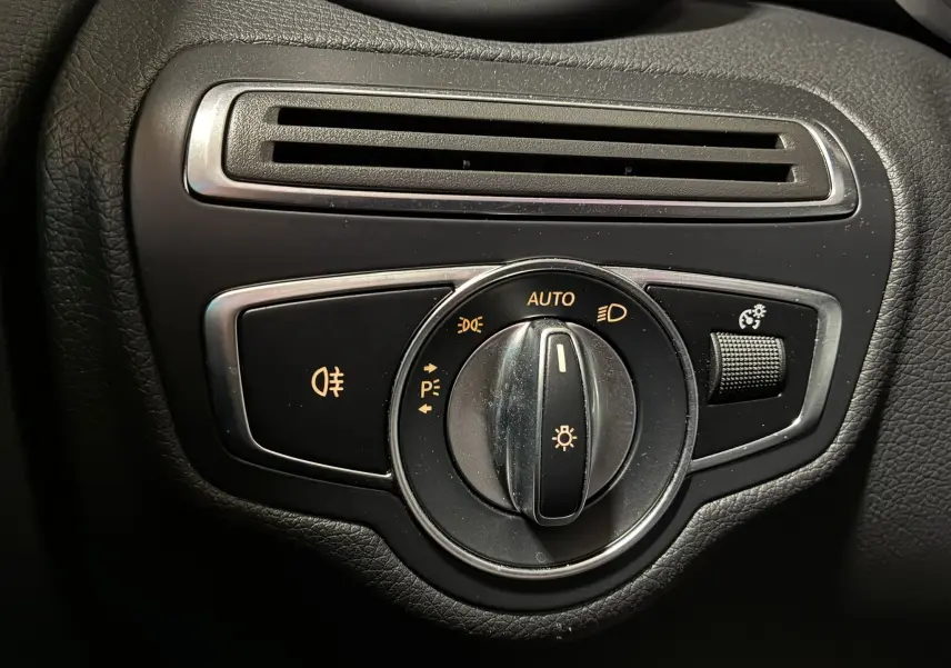 Gros plan sur la commande des feux avec molette et réglage d’intensité dans l’habitacle noir d’une Mercedes Classe C Break 220D AMG Line.