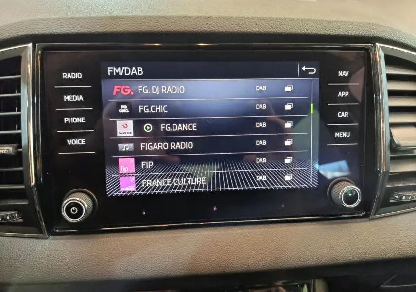 Écran tactile central du tableau de bord du Skoda Karoq blanc 2024 affichant les stations radio FM/DAB.