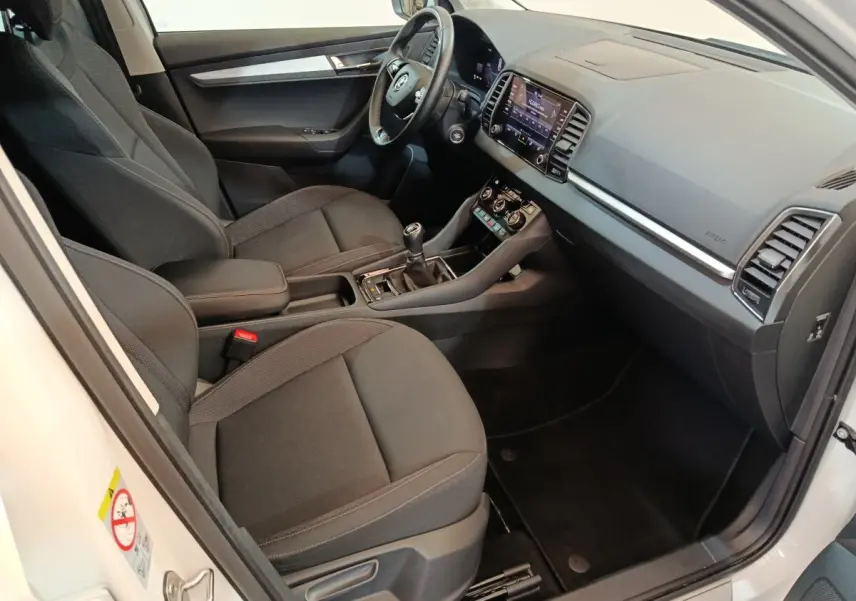Vue intérieure côté conducteur du Skoda Karoq blanc 2024, montrant sièges noirs, volant cuir et écran tactile central.