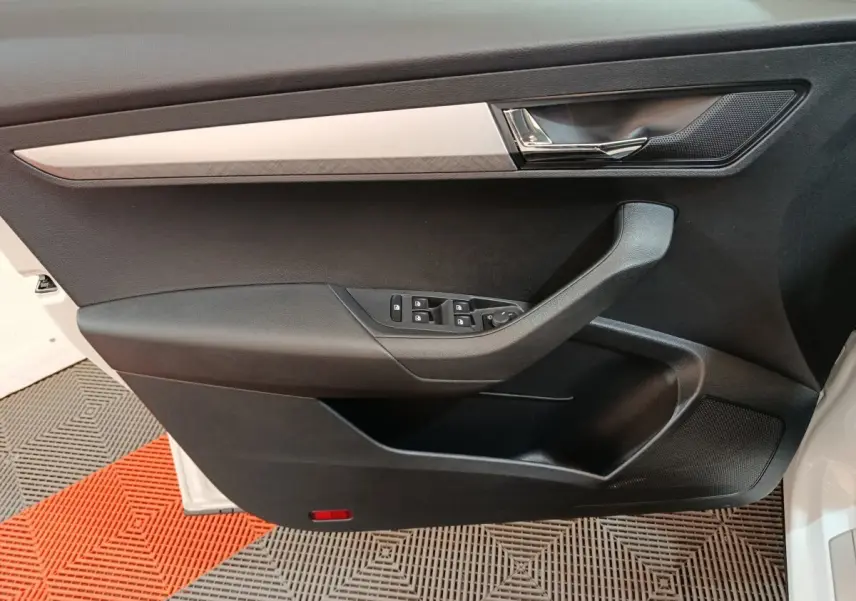 Vue rapprochée de la porte avant gauche noire du Skoda Karoq blanc, avec commandes de vitres et poignée chromée.